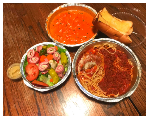 A wooden table topped with bowls of food including spaghetti , soup , salad and garlic bread. | Walt's Auto Service