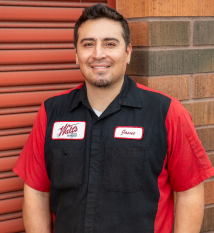 A man in a red and black shirt is standing in front of a brick wall. | Walt's Auto Service