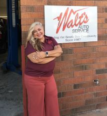 A woman is standing in front of a walt 's auto service sign. | Walt's Auto Service