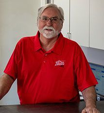 A man with a beard and glasses is sitting at a counter wearing a red shirt.