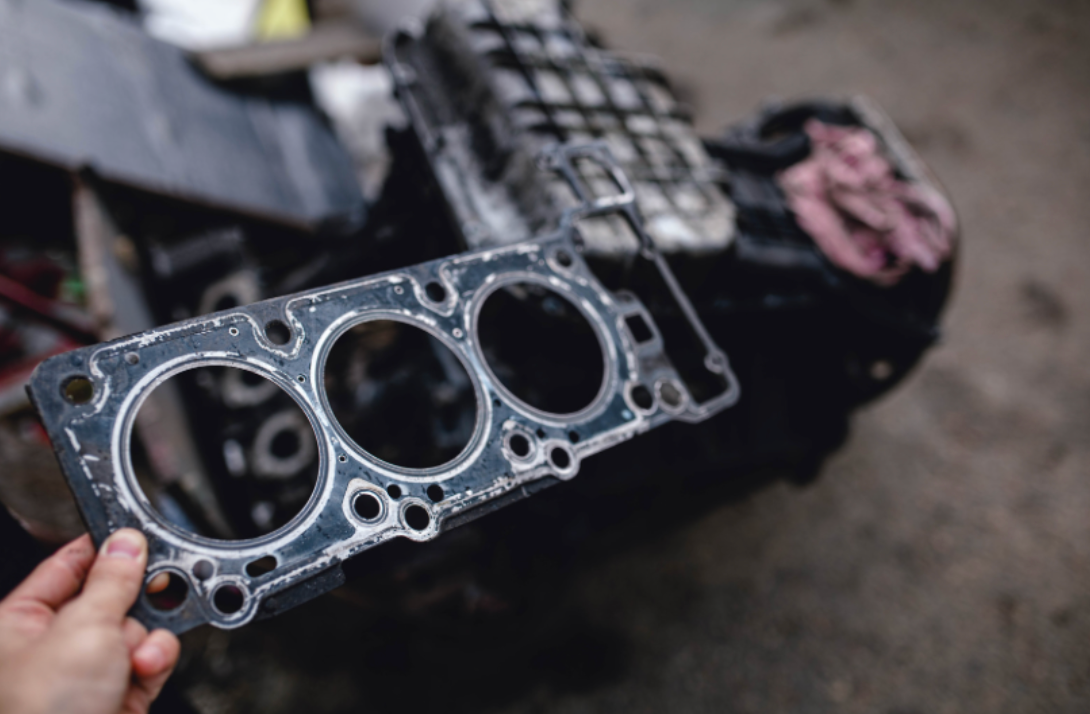 A person is holding a head gasket in front of a motorcycle engine. | Walt's Auto Service