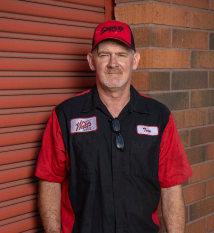 A man wearing a red hat and a black shirt is standing in front of a brick wall. | Walt's Auto Service
