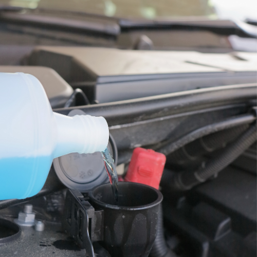 A bottle of blue liquid is being poured into a black cup | Walt's Auto Service