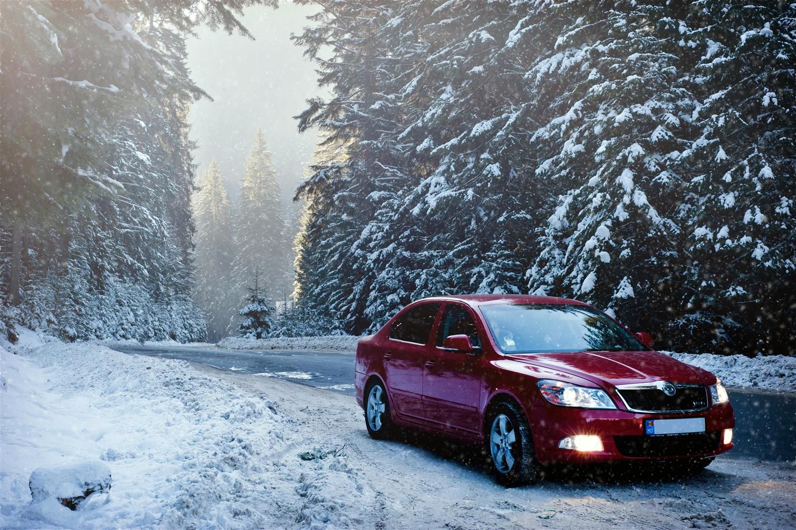 A red car is driving down a snowy road in the woods. | Walt's Auto Service