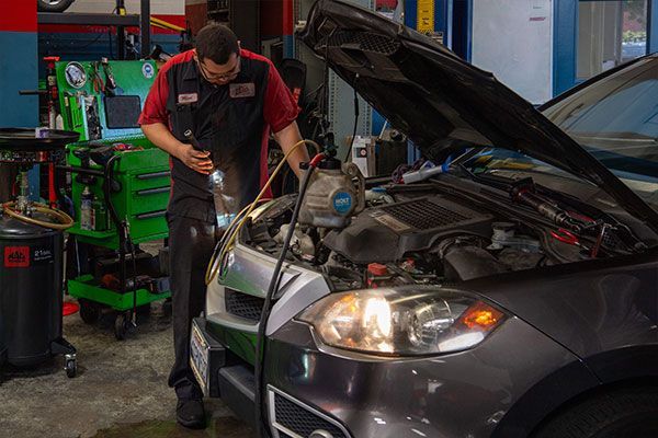 A man is working on a car in a garage with the hood open. | Walt's Auto Service