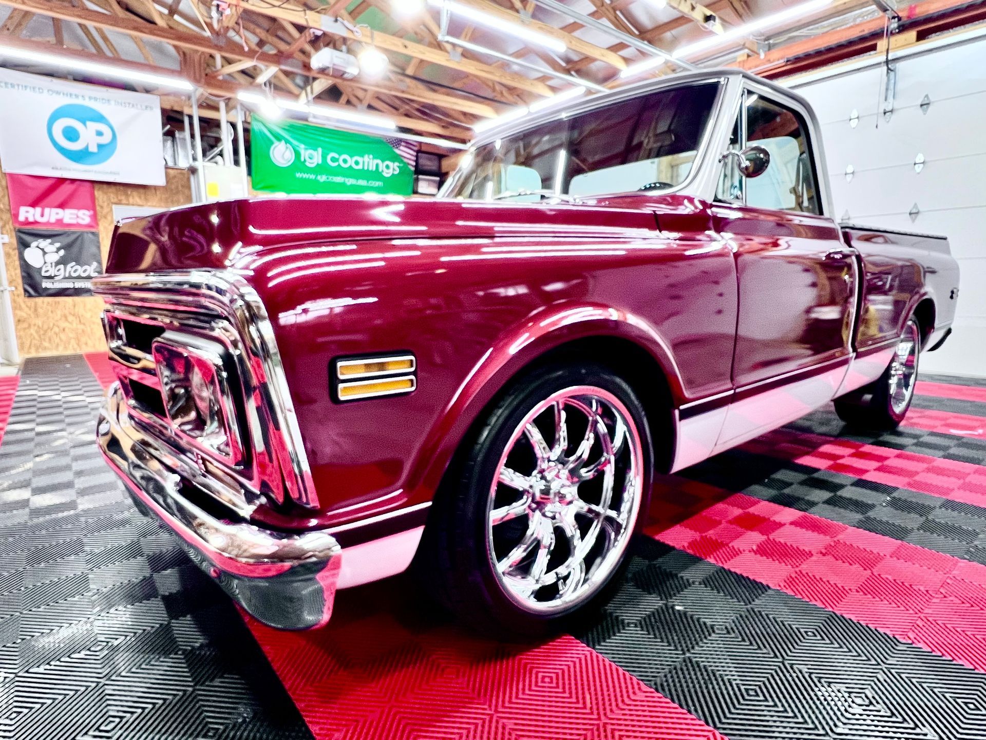 Burgundy and white classic Chevy pickup truck on a red and black tiled garage floor.