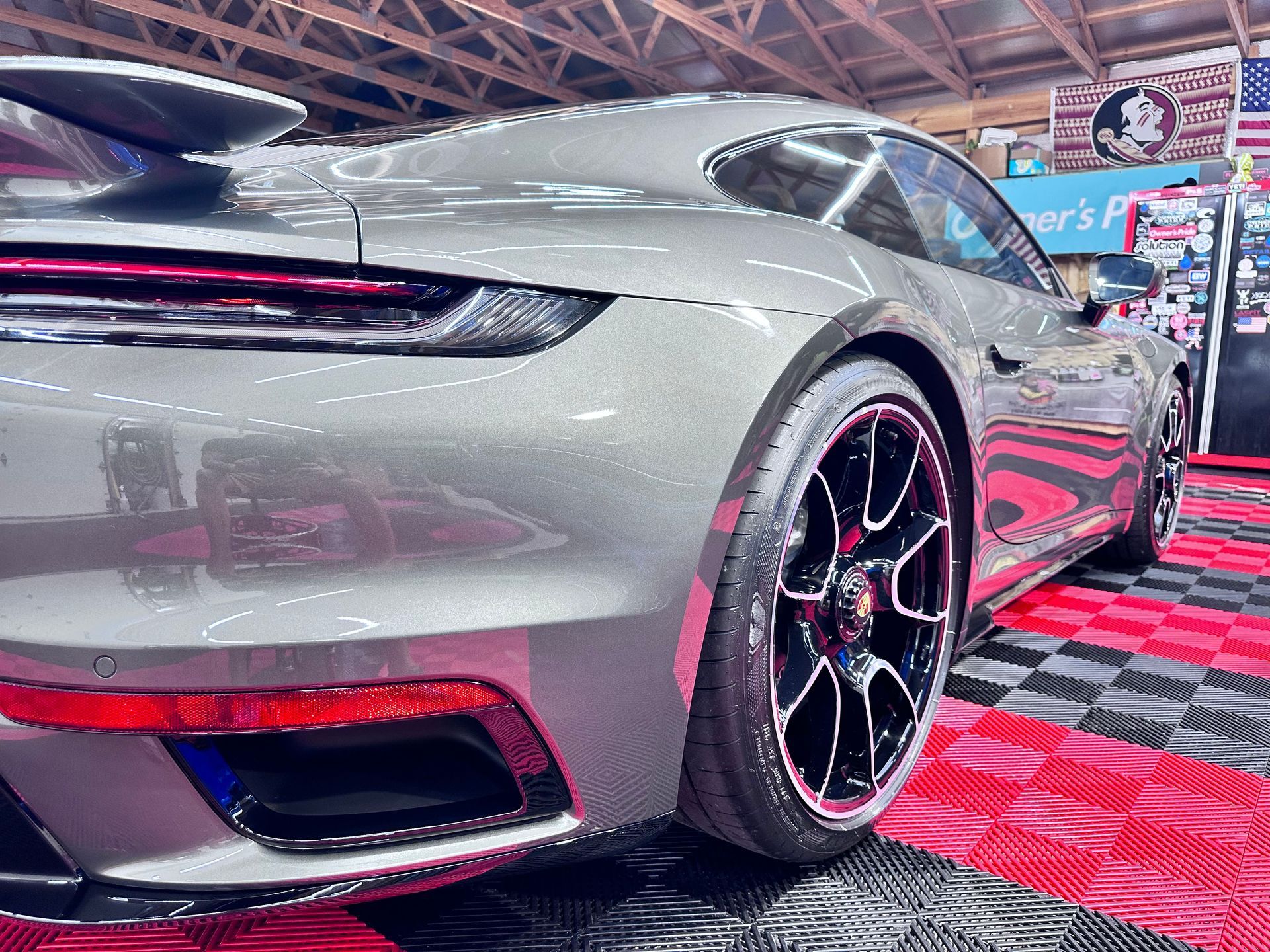Gray Porsche sports car parked on a checkered floor at an event, with black and red accents.