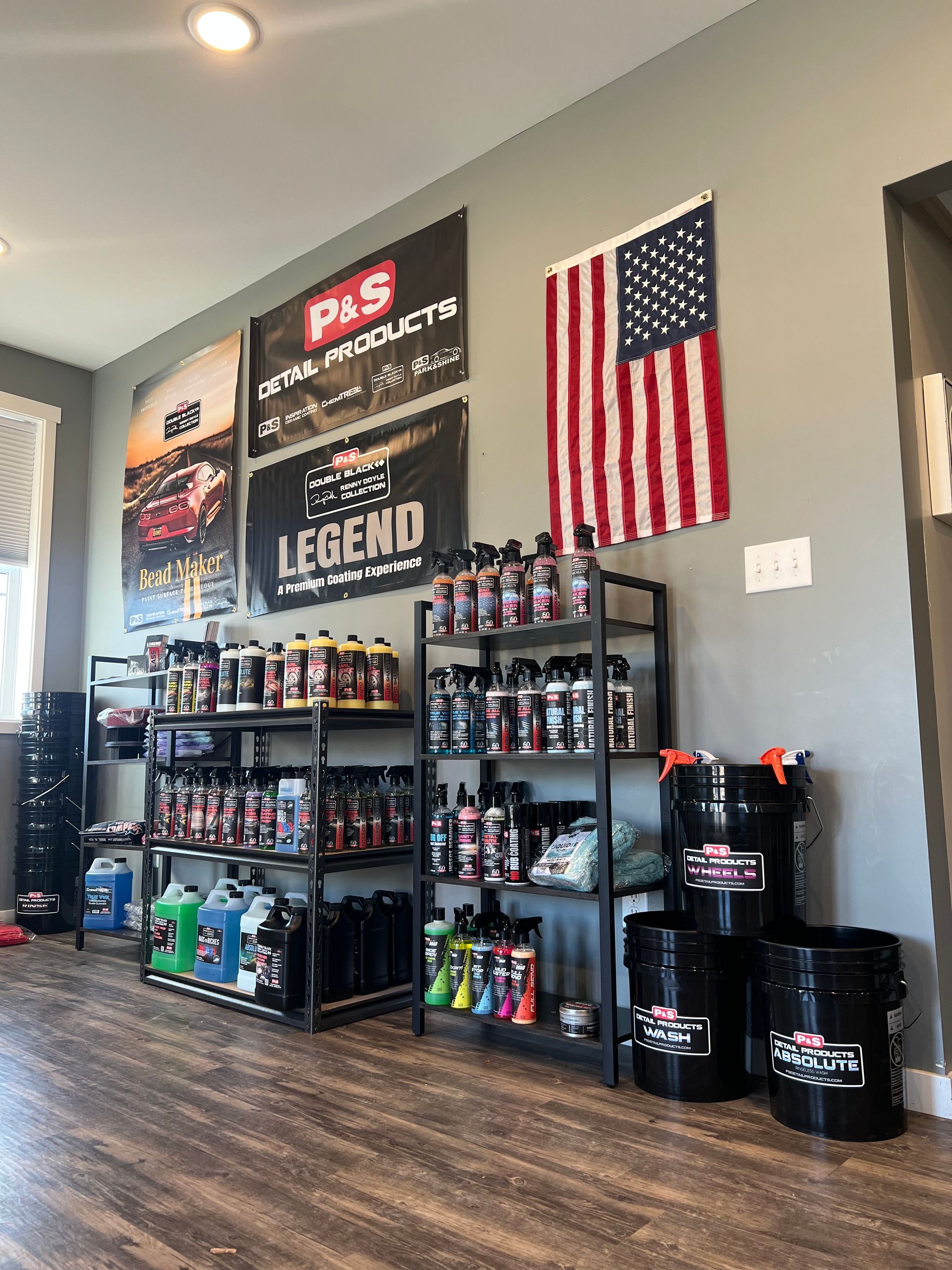 Car detailing supplies displayed on shelves in a shop, with an American flag and promotional banners on the wall.