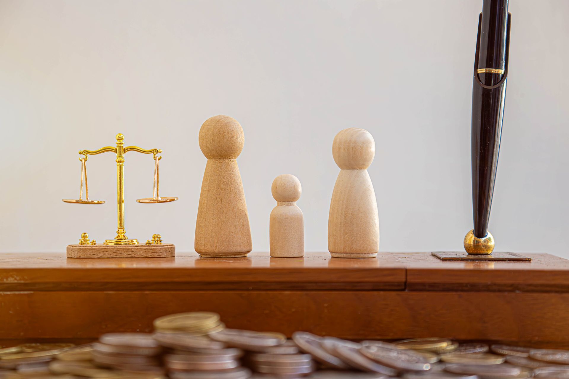 Wooden justice scales and figurines on a desk, with a gavel at right and stacked coins in front