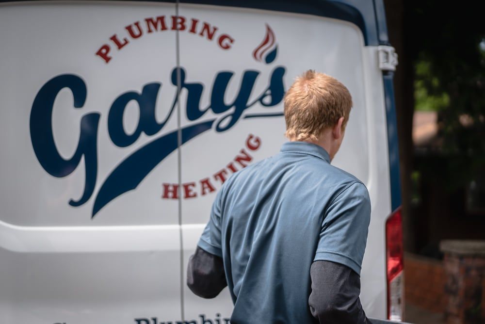 A man is standing in front of a gary 's plumbing and heating van.