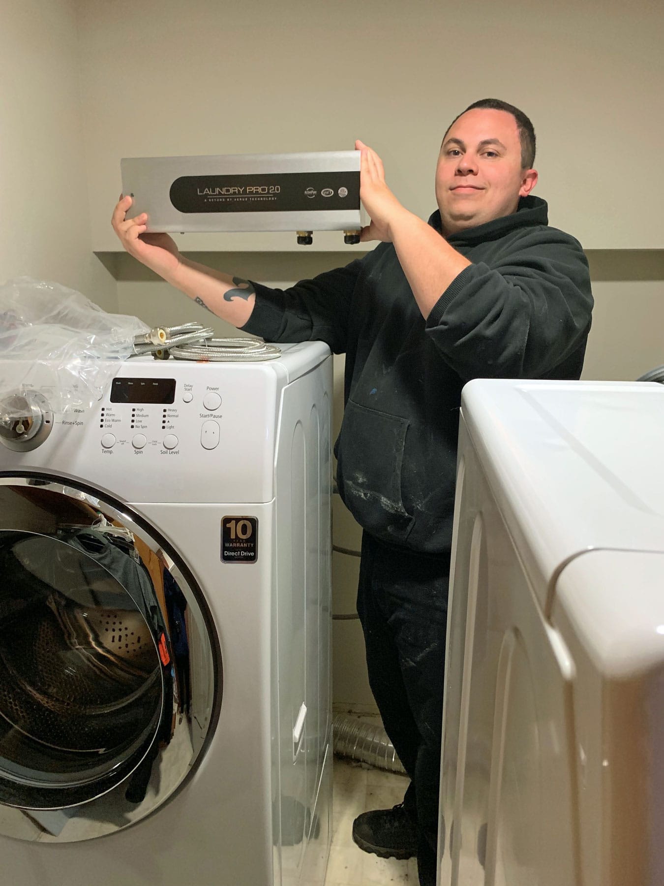 A man is standing next to a washing machine and dryer in a laundry room.