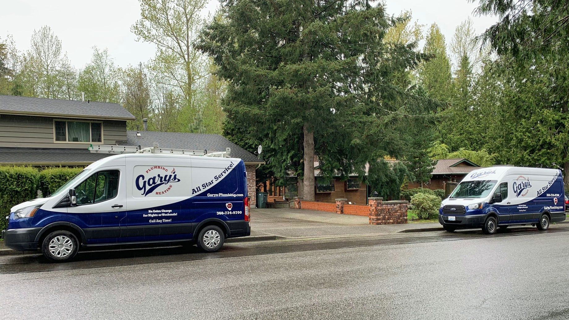 Two blue and white vans are parked in front of a house.