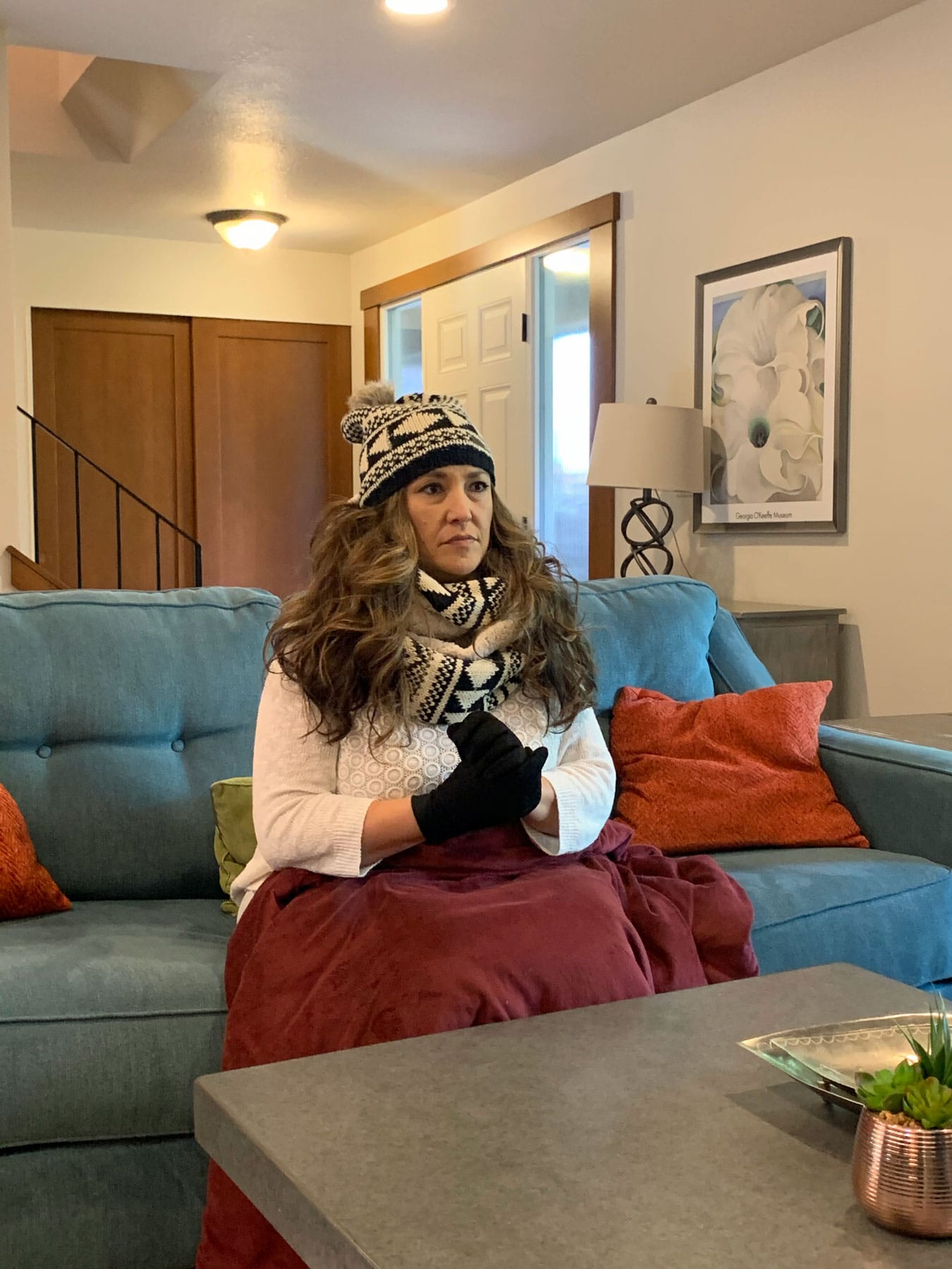 A woman is sitting on a couch wearing a hat and scarf.
