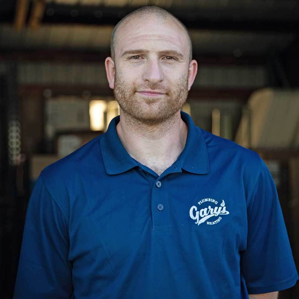 A bald man with a beard is wearing a blue polo shirt that says garry 's on it.