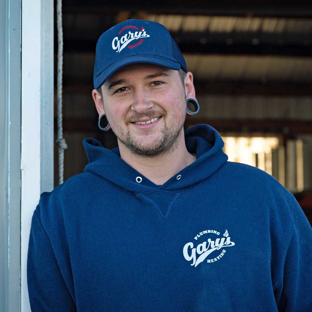 A man wearing a blue hat and a blue hoodie is standing in front of a window.