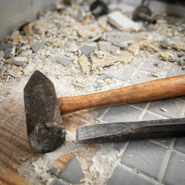 A hammer and a chisel are laying on a tiled floor