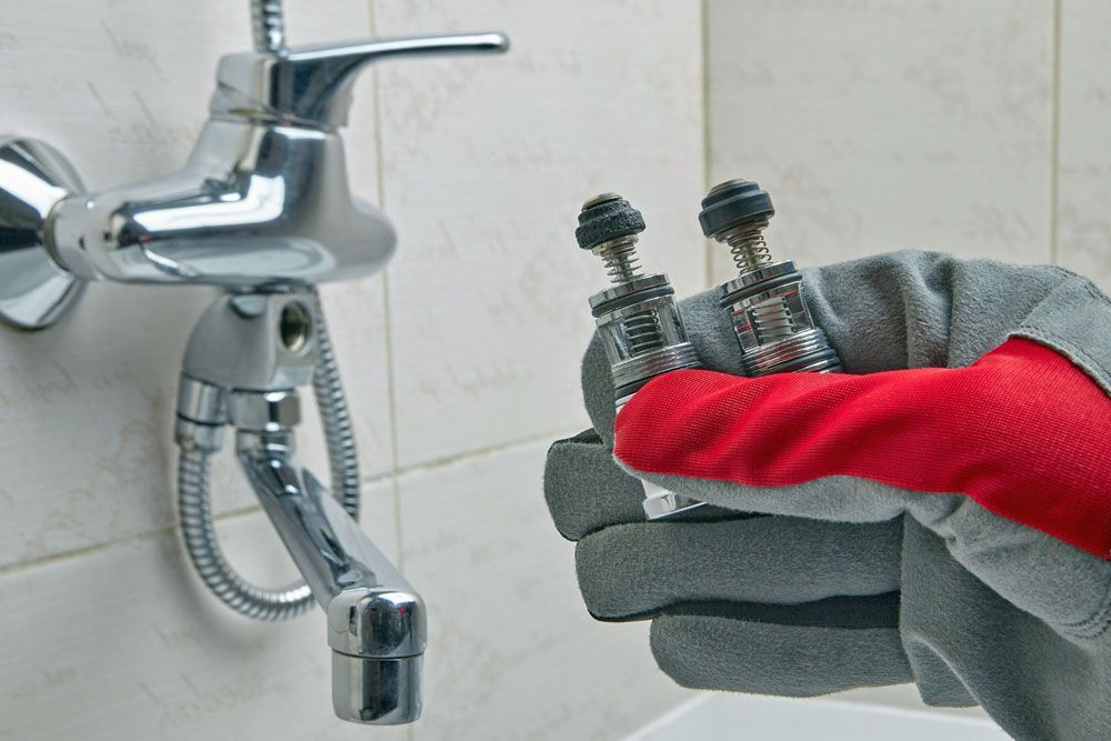 A person is holding a pair of screws in front of a bathroom faucet.
