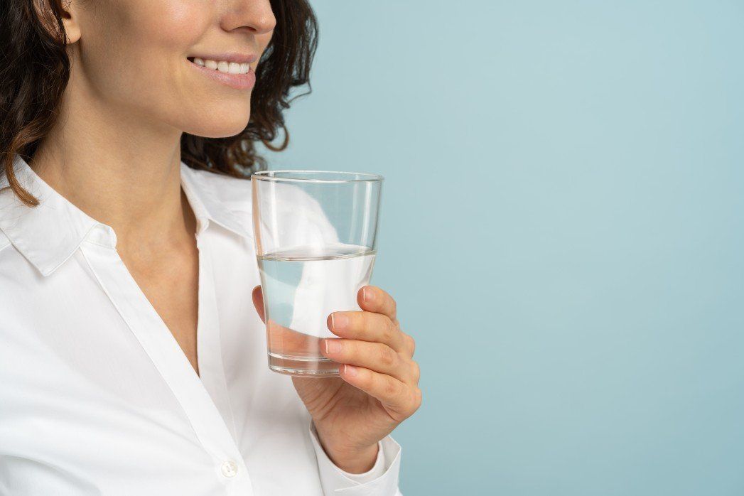 A woman in a white shirt is drinking a glass of water.
