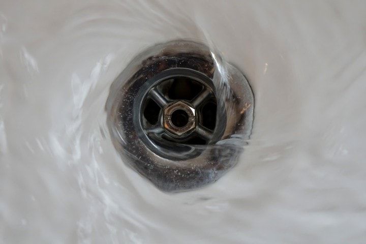 Water is running down a drain in a bathroom sink.