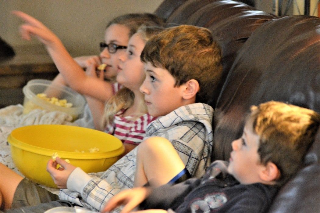 A group of children are sitting on a couch eating popcorn