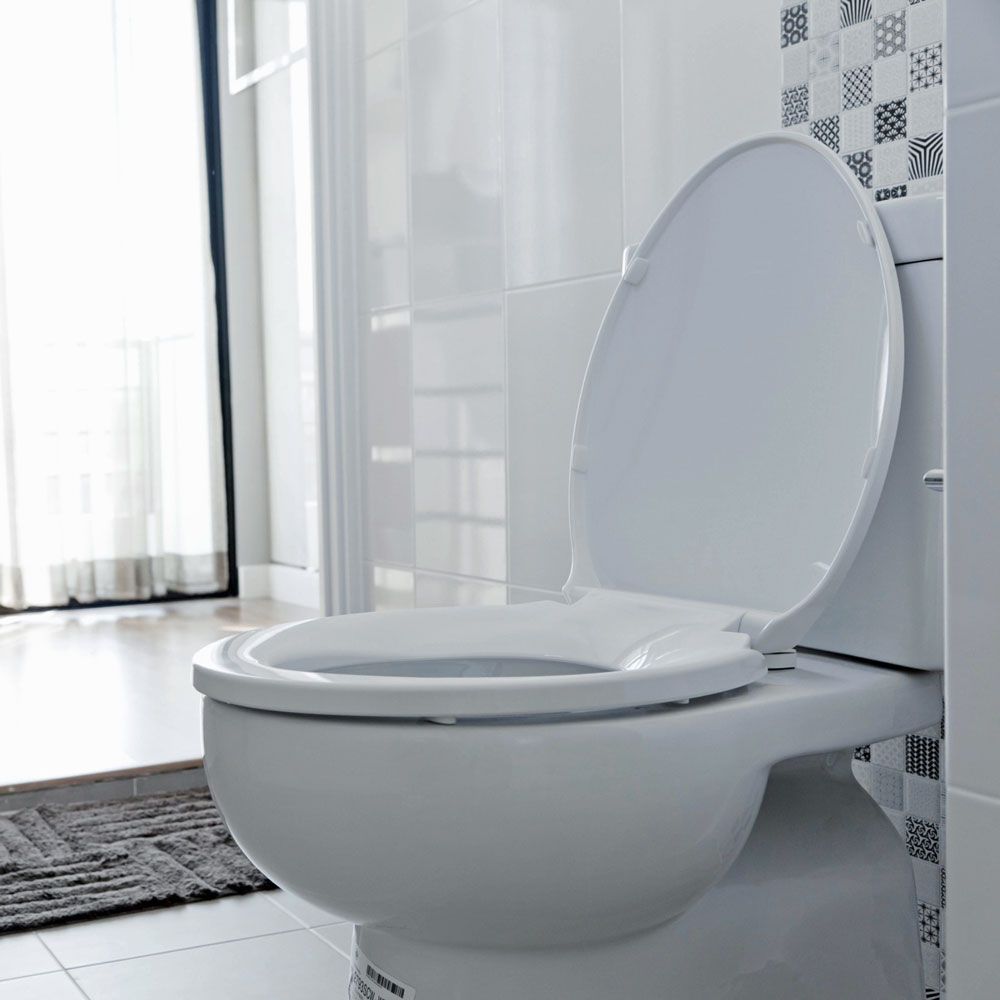 A white toilet is sitting in a bathroom next to a window.