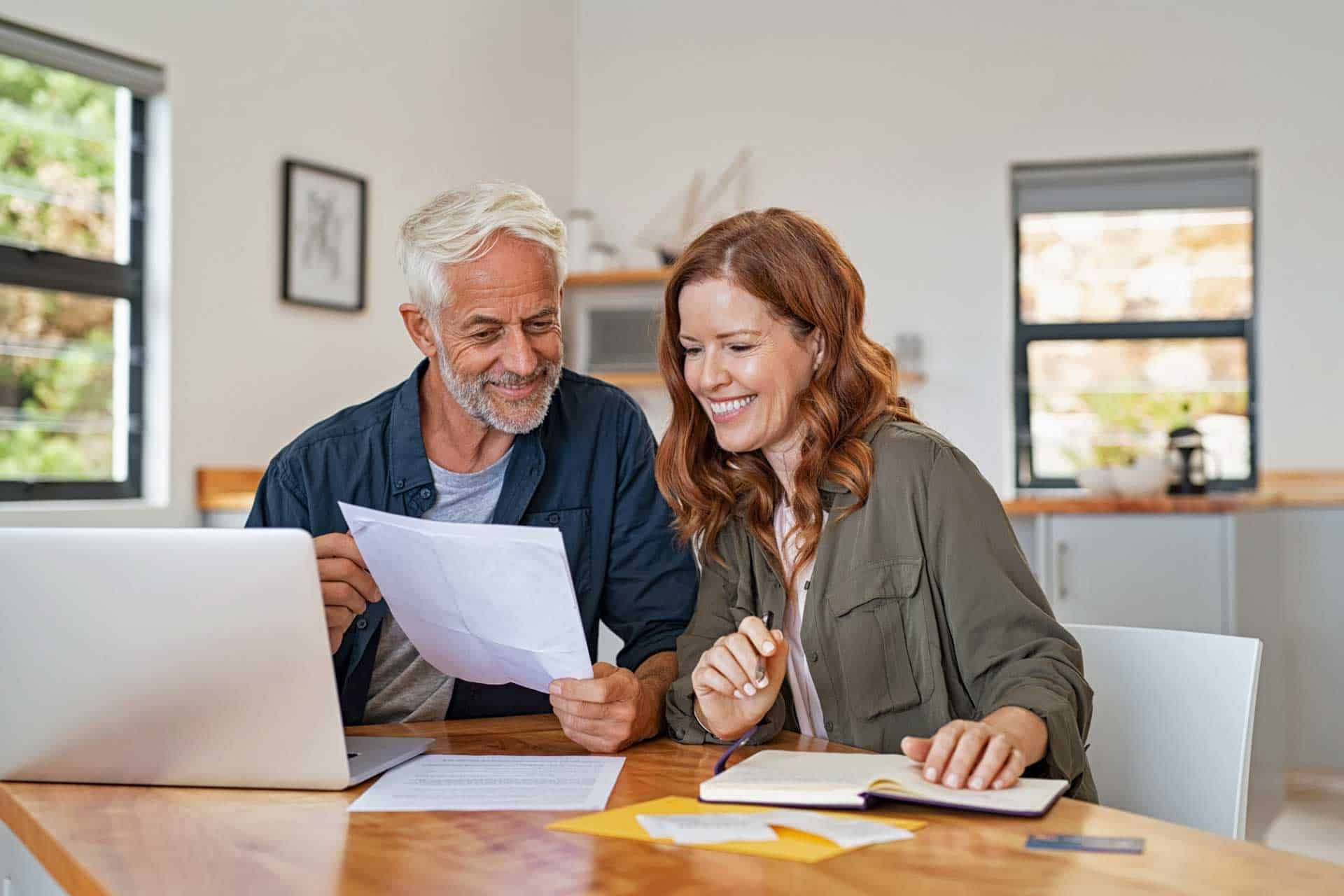 A man and a woman are sitting at a table looking at papers and a laptop.