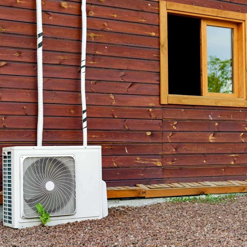A fan is sitting outside of a wooden house next to a window.