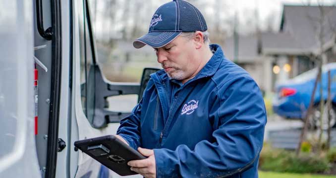 A man is standing in front of a delivery truck looking at a tablet.