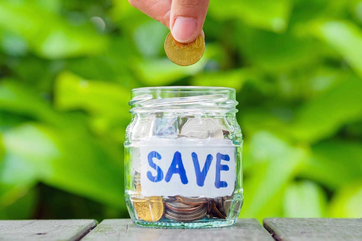 A person is putting a coin into a jar that says `` save ''.