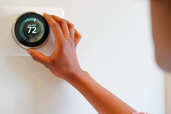 A person is adjusting a smart thermostat on a wall.
