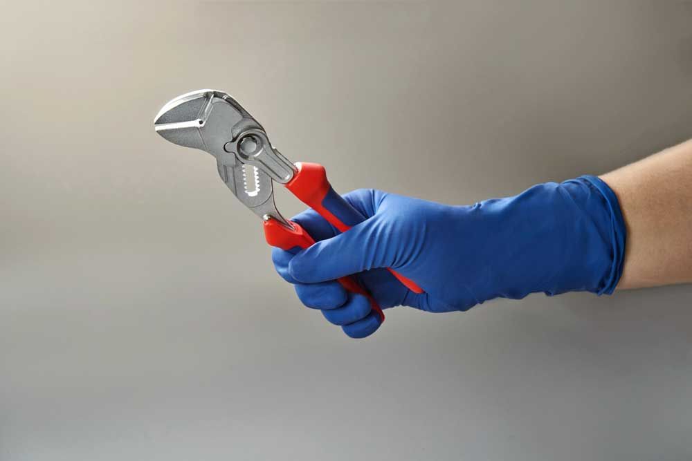 A person wearing blue gloves is holding a wrench.