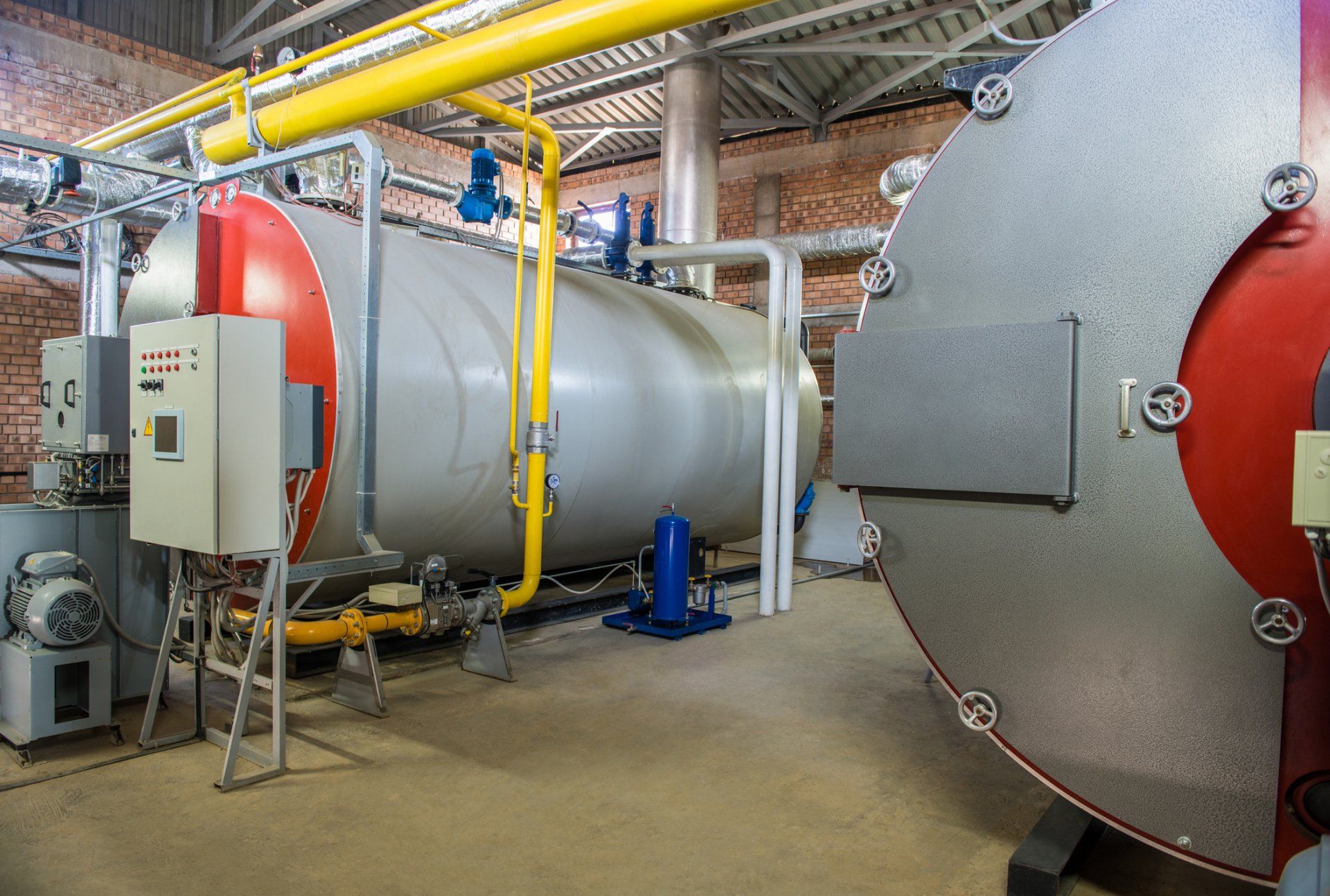 Large industrial boiler and ductwork in a utility room with pipes, controls, and red end caps