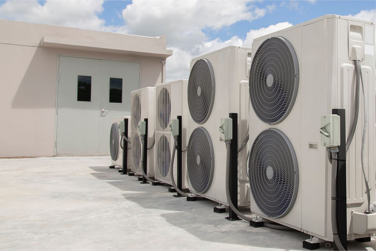 Row of white outdoor HVAC units beside a beige building under a partly cloudy sky
