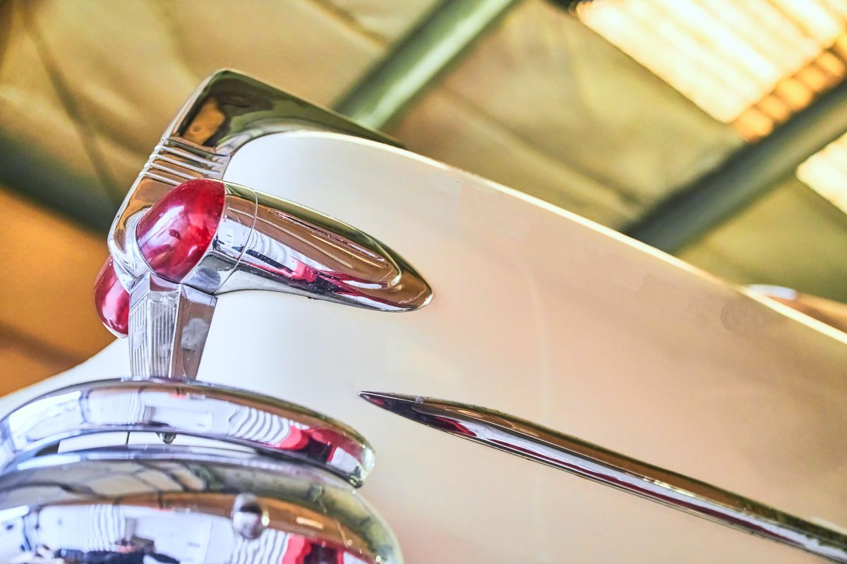 Close-up of a classic car tail fin, chrome details and red taillight against white paint. | Priced Right Auto Clinic