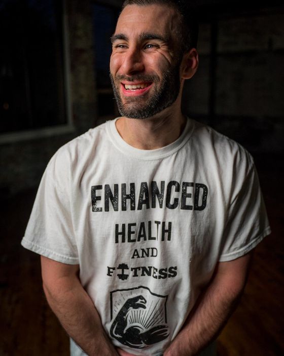 A man wearing a white t-shirt that says enhanced health and fitness