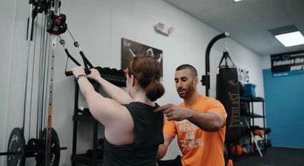 A man is teaching a woman how to use a machine in a gym.