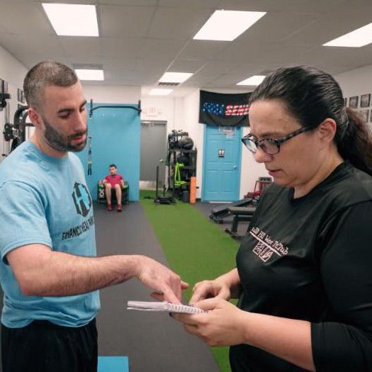 A man and a woman are standing in a gym looking at a piece of paper.