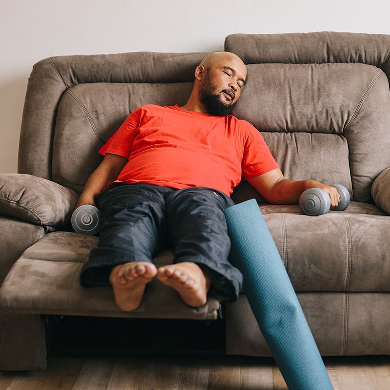 A man is sleeping on a couch while holding dumbbells