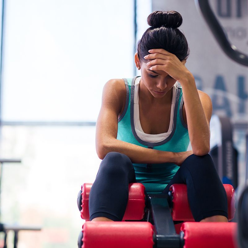A woman is sitting on a machine in a gym with her hand on her head.