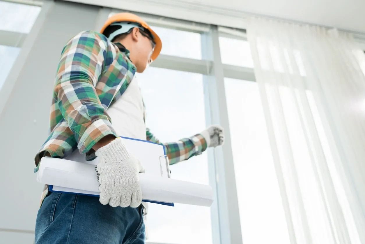 A man wearing a hard hat and gloves is holding a blueprint in a room.
