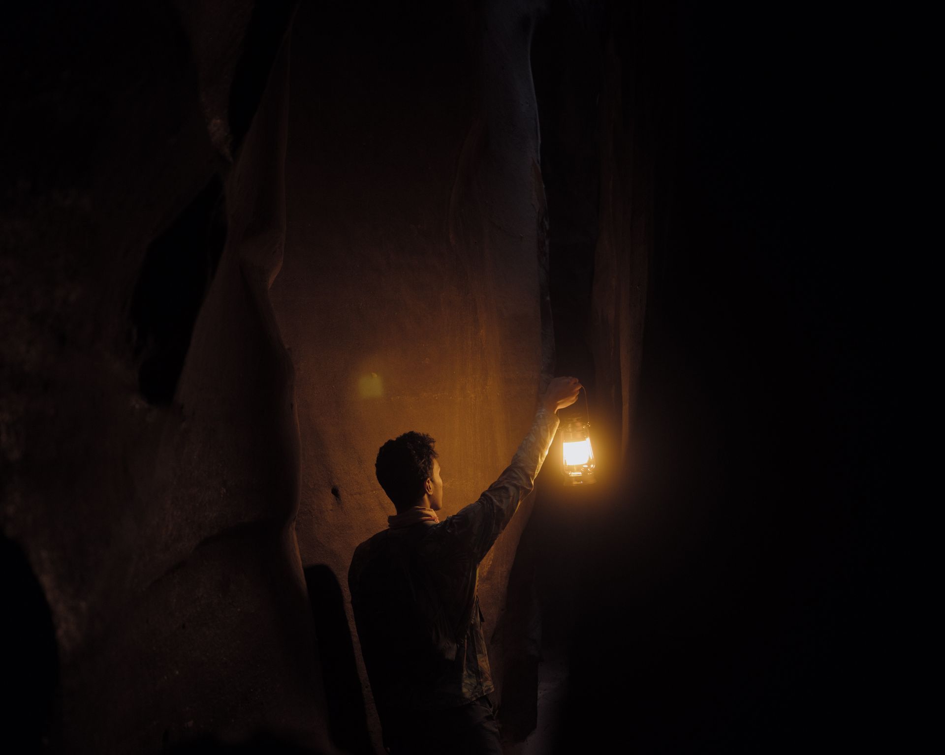 man searching in dark cave holding a lamp in right outstretched arm