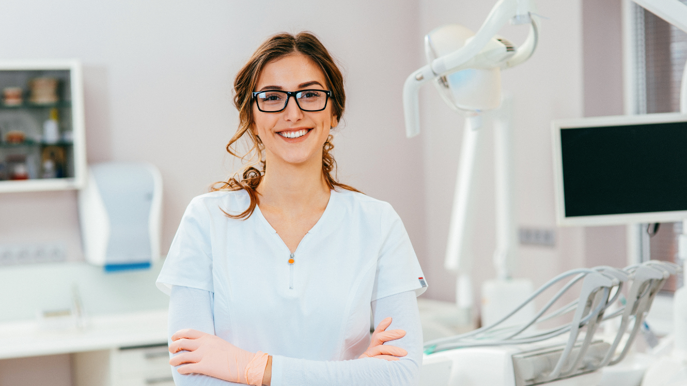 a female dentist is smiling in a dental office with her arms crossed .