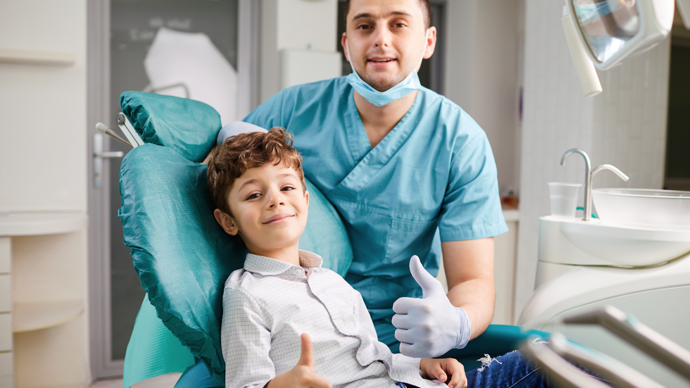 a young boy is sitting in a dental chair and giving a thumbs up .