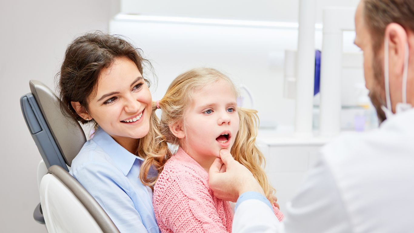 a woman and a little girl are sitting in a dental chair talking to a dentist .