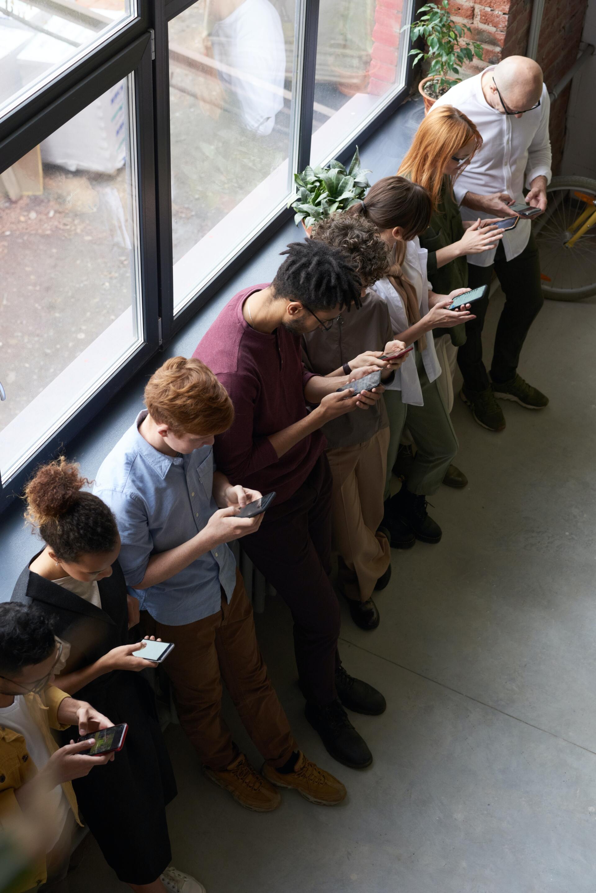 a group of people are standing in front of a window looking at their phones .