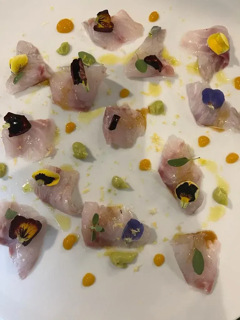 Un piatto bianco sormontato da una varietà di cibo e fiori.