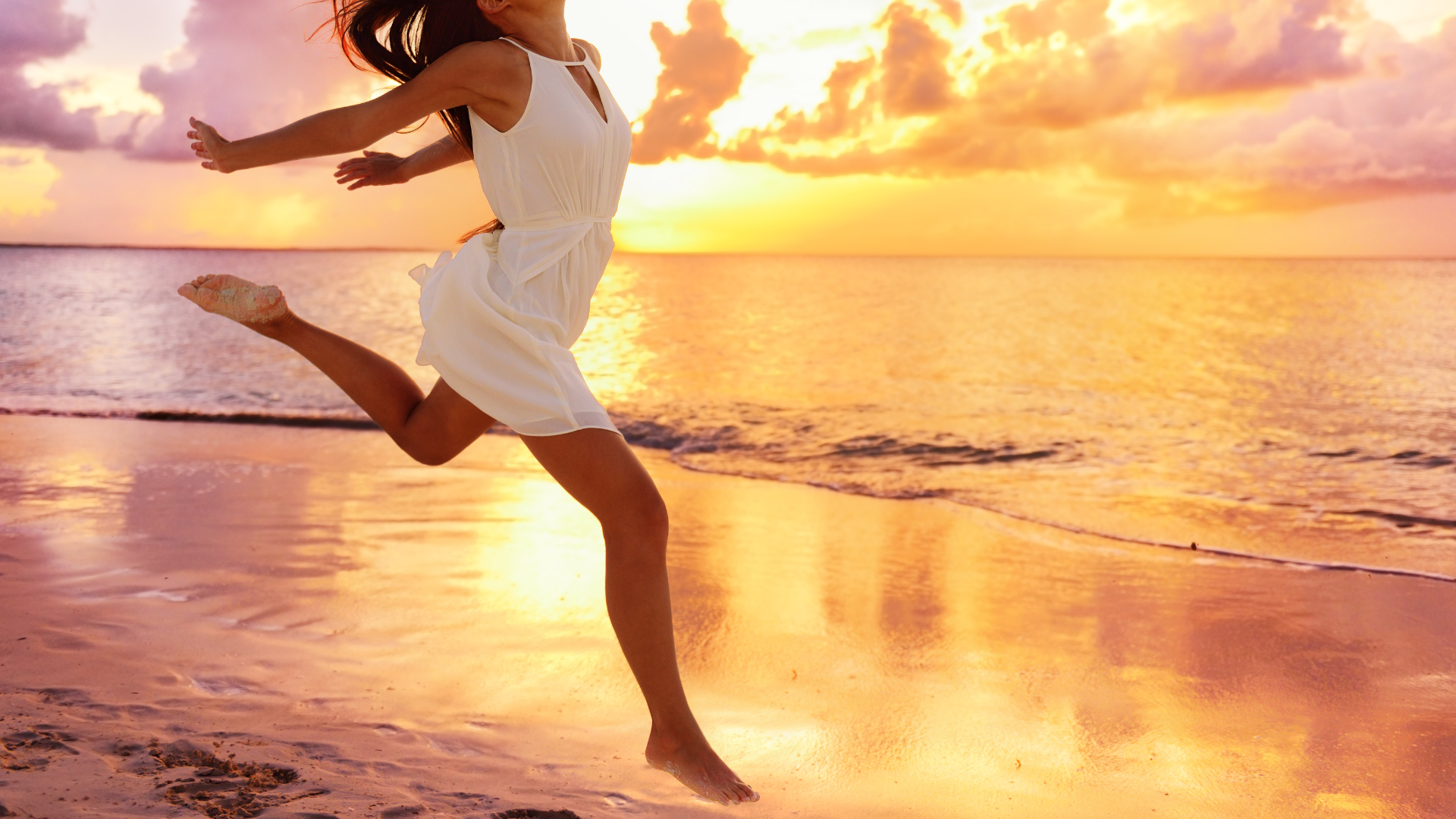 Woman in white dress jumps joyfully on beach at sunset.