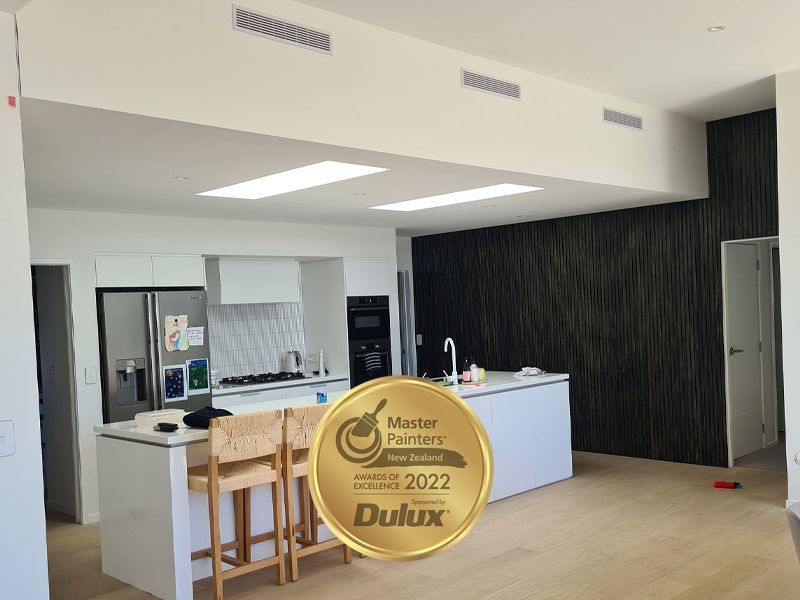 Kitchen with white cabinets, island, and black accent wall; Master Painters Award 2022 seal is visible.