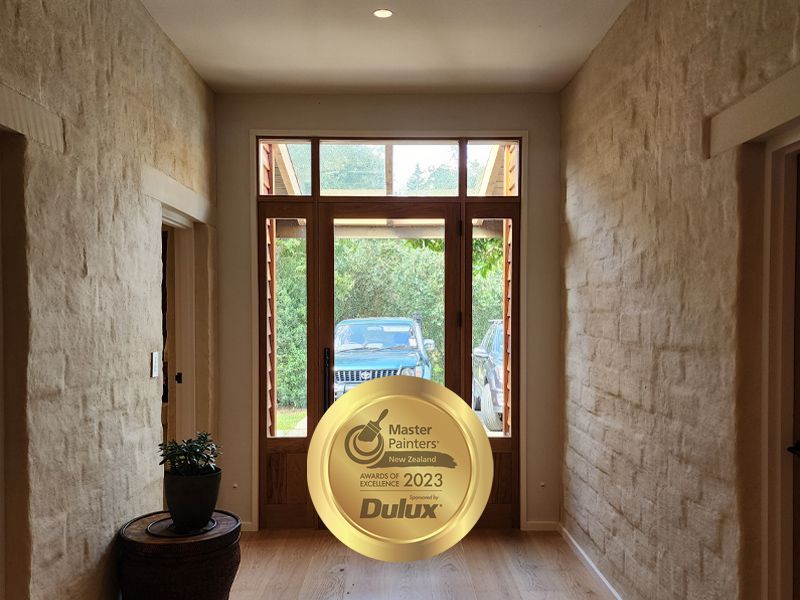 Hallway with brick-textured walls, wooden door with window, and a Dulux Master Painter award.