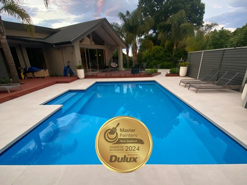 Pool with blue water, surrounded by white concrete, house in background. Dulux Master Painters award badge.
